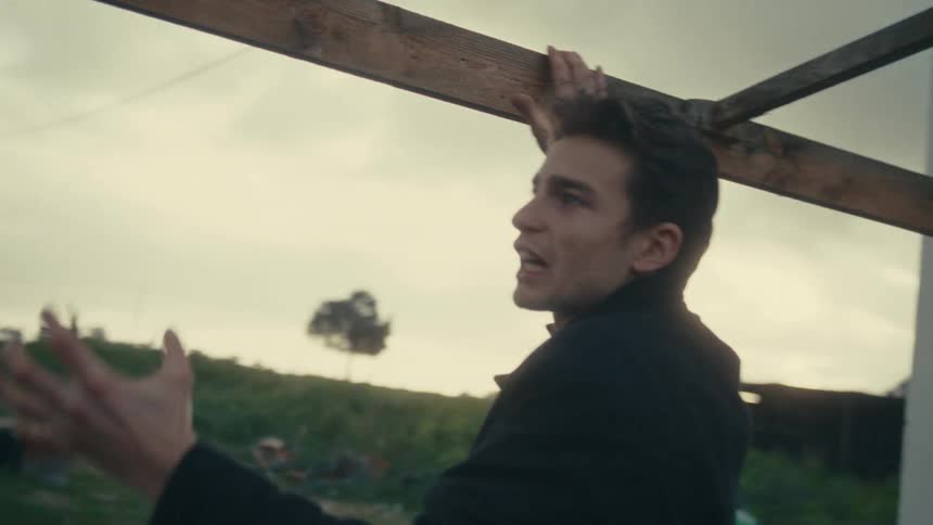 Man outdoors gesturing intensely while holding a wooden structure