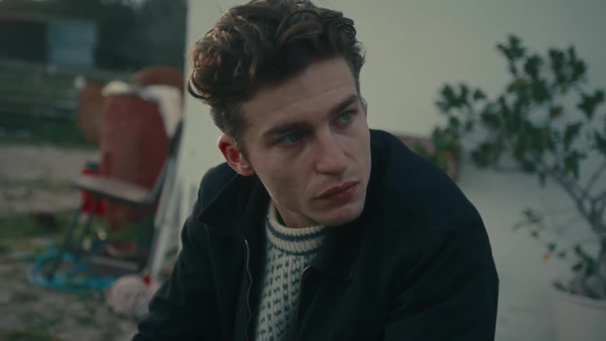 Young man sitting outside next to a house turns his head