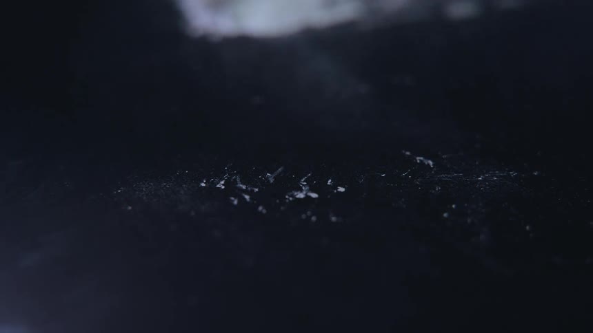 A pile of white powdery substance being blown away from a dark reflective surface