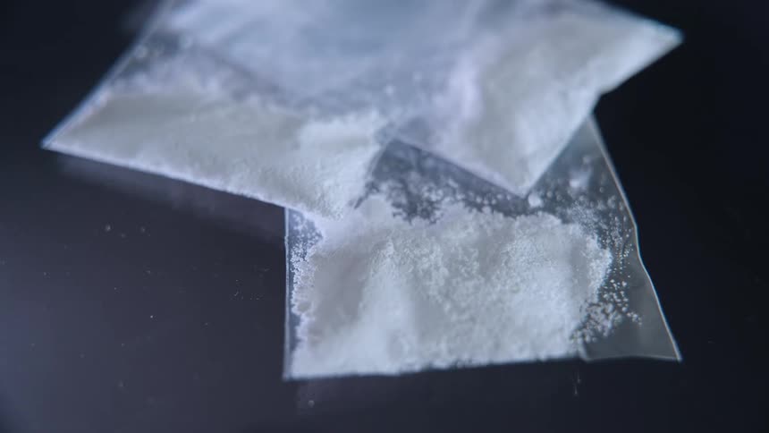 Several small plastic baggies filled with a white granular powder resting on a dark surface