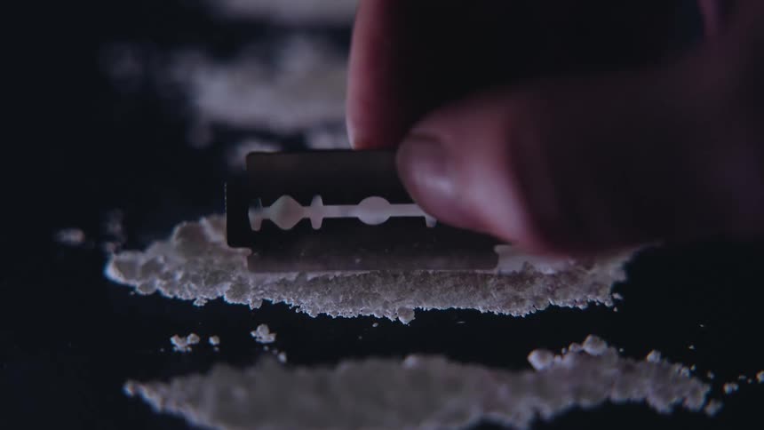 Hand with a razor blade dividing powder