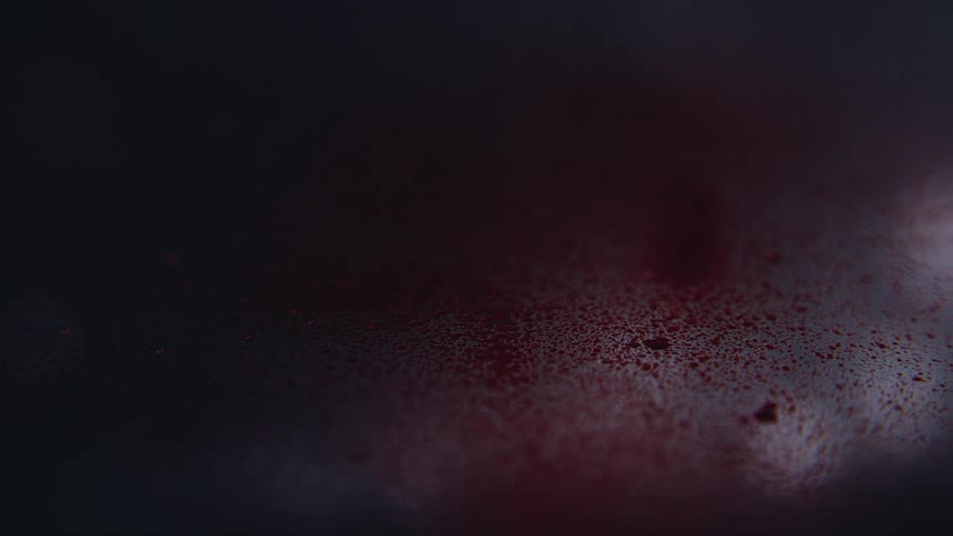 A dark red powder is dusting onto a blurred silver surface leaving speckles of dust scattered