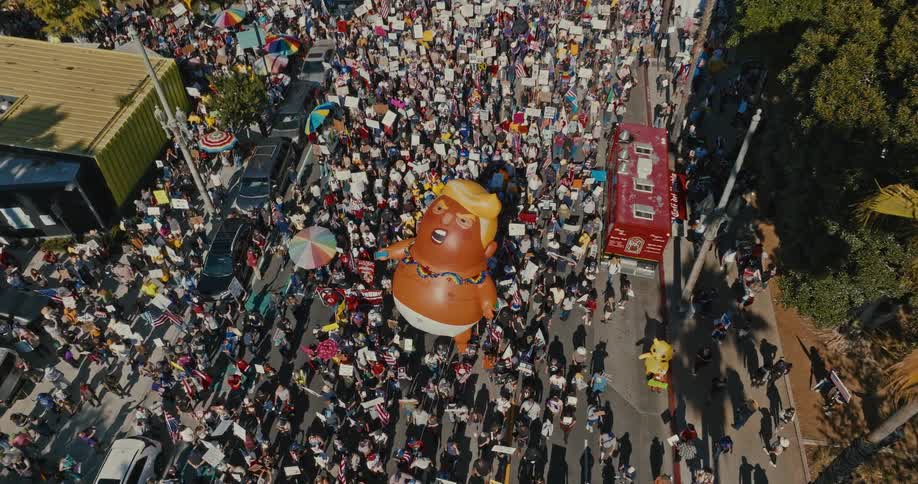 Protesters are marching down a street with a large political balloon