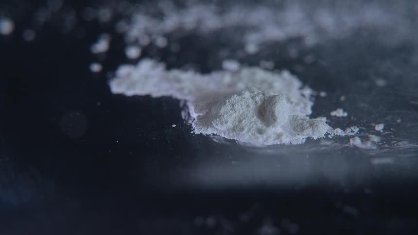 A closeup dim view captures a small pile of white powder scattered across a dark reflective surface its grains catching the light