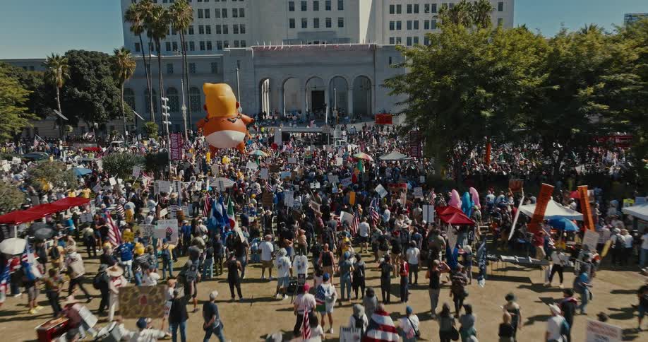 A large group of people is gathered in a city park to protest
