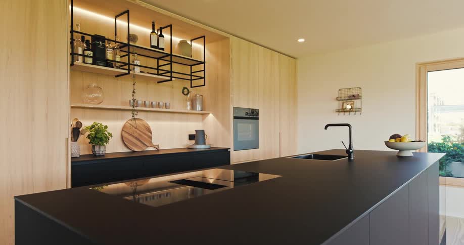 A sleek modern kitchen featuring matte black countertops and an island contrasted with light wood cabinetry and open shelving