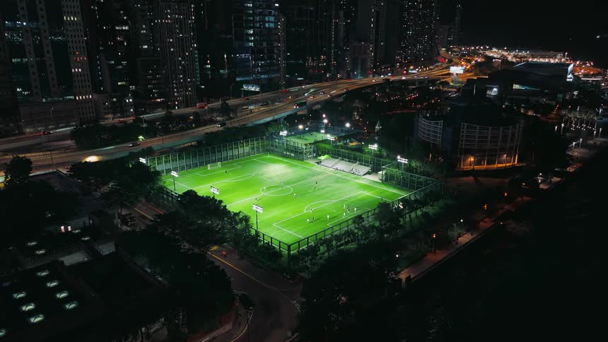 Nightlit soccer field stands out with players amid the cityscape