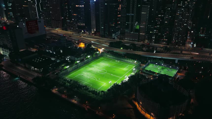 Illuminated soccer field at night surrounded by buildings and highways