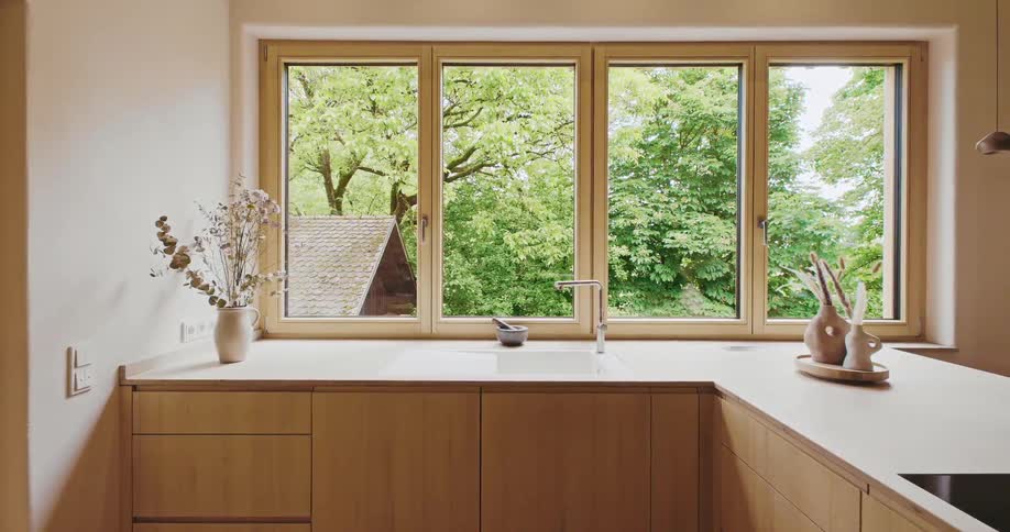 Minimalist kitchen with wooden furniture receives natural light from large windows
