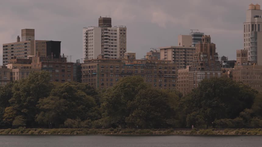 Old buildings line up behind a strip of trees by the waterfront