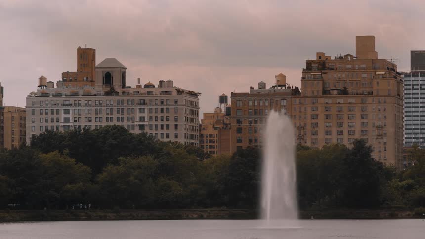 Fountain jet rises in front of residential buildings surrounded by trees