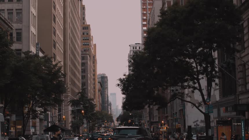 Busy traffic and pedestrians cross an avenue lined with tall buildings