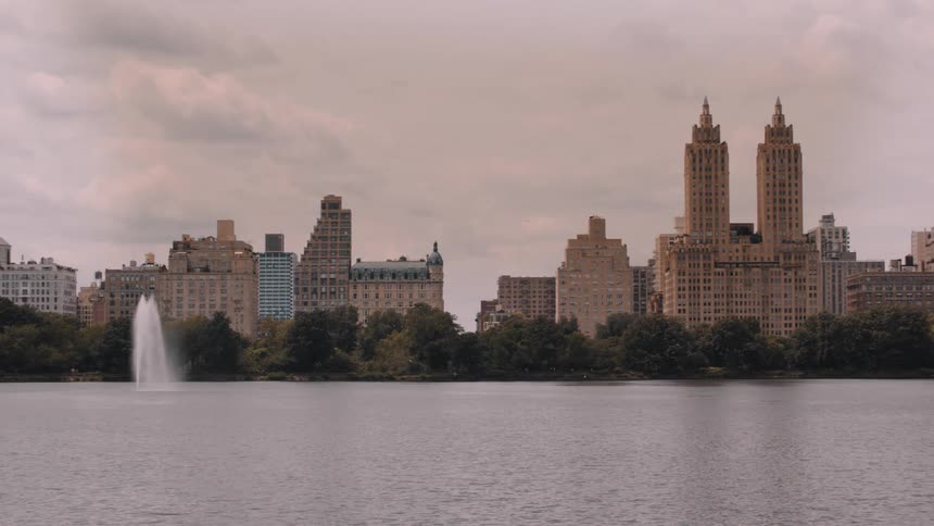 Water fountain rises in front of historic buildings by an urban lake