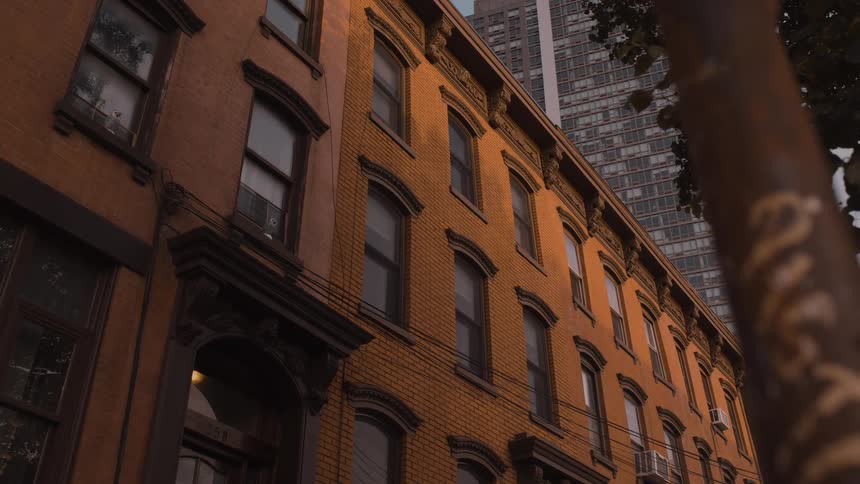 Historic brick townhouses glow in the warm light of dusk standing in stark contrast to a modern skyscraper towering behind them