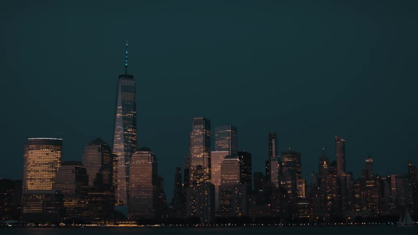 Airplane flying over illuminated skyscrapers reflecting nighttime lights on the riverbank