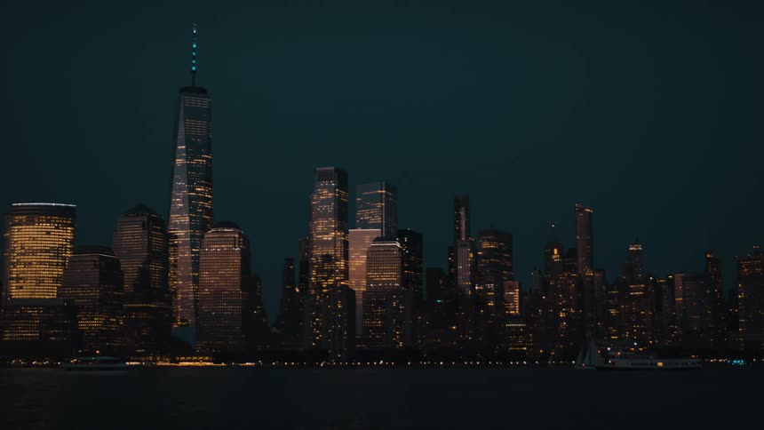 Lights glow on towers and skyscrapers on the metropolitan coast as boats sail on the water at night