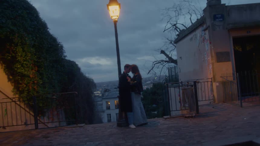 A young couple holding each other romantically while standing together at the top of a stairway outdoors at dusk