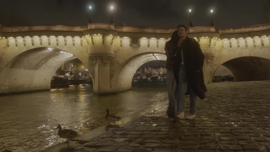The man and woman are hugging as they walk by the canal