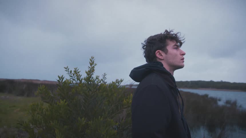 Man gazes at the horizon near a lake under a cloudy sky