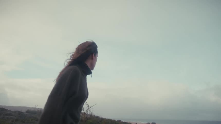 Woman screams facing the sea amid the wind and coastal landscape