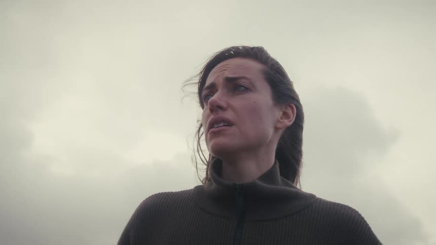 Woman faces the horizon with an anguished expression under the cloudy sky