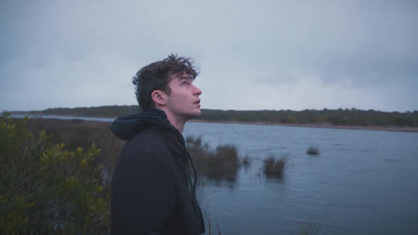 Man quietly gazes at the lake under the gray calm sky