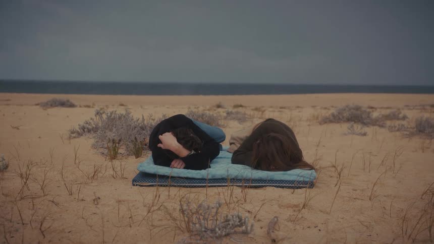 Two people lying side by side on a blanket over deserted sand