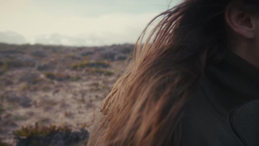The wind is blowing the womans hair on the beach