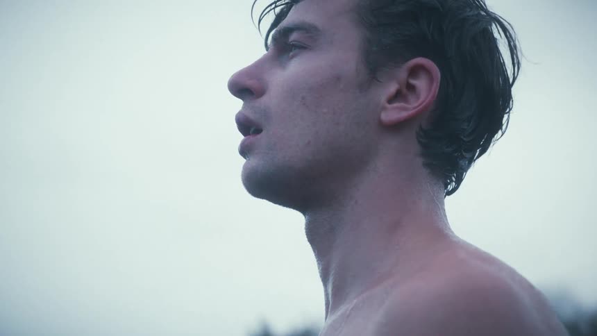 Shirtless man gazes at the horizon under cold cloudy light