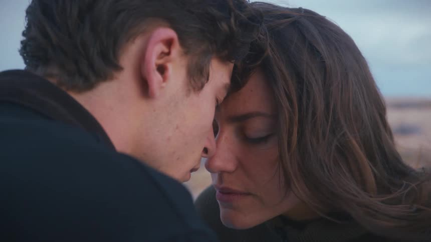 Young couple outdoor resting their forehead against each other as wind blows the womans hair both eyes aare shut in a romantic moment
