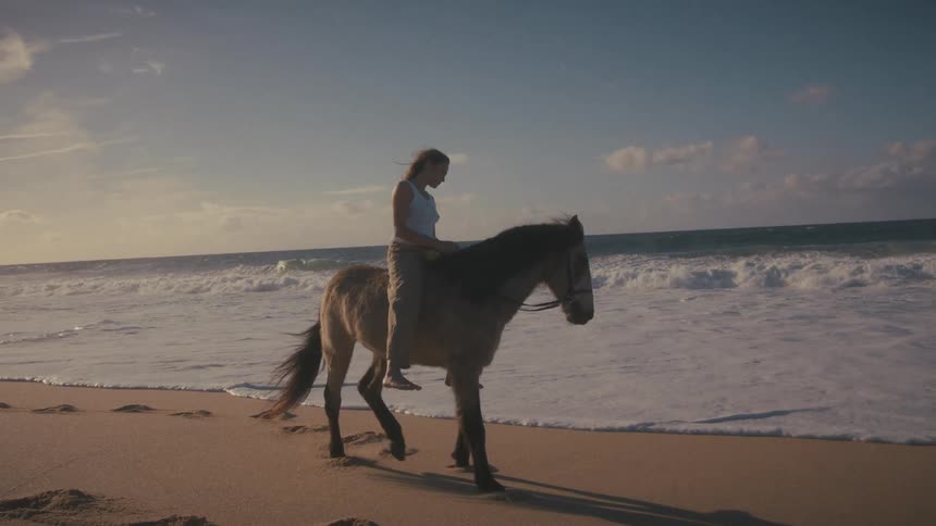 Woman rides barefoot along the beach at sunset