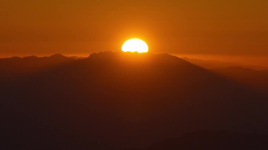 Sun sets behind the mountains painting the sky in deep orange hues