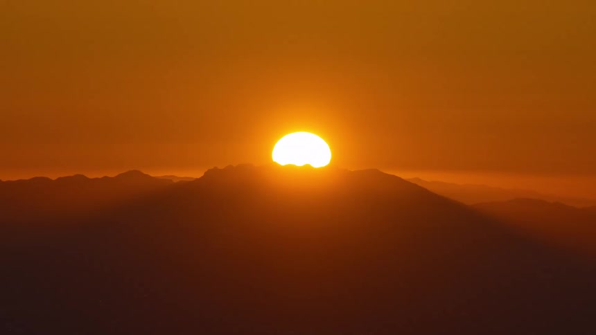 A glowing sun sinks behind distant mountains casting warm orange light across the hazy horizon