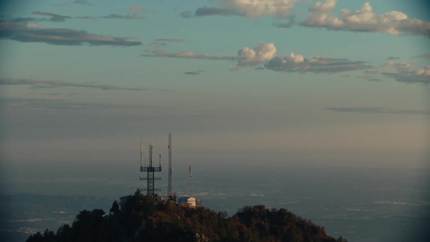 An antenna atop a hill covered in trees with a vast horizon in the background on a cloudy day