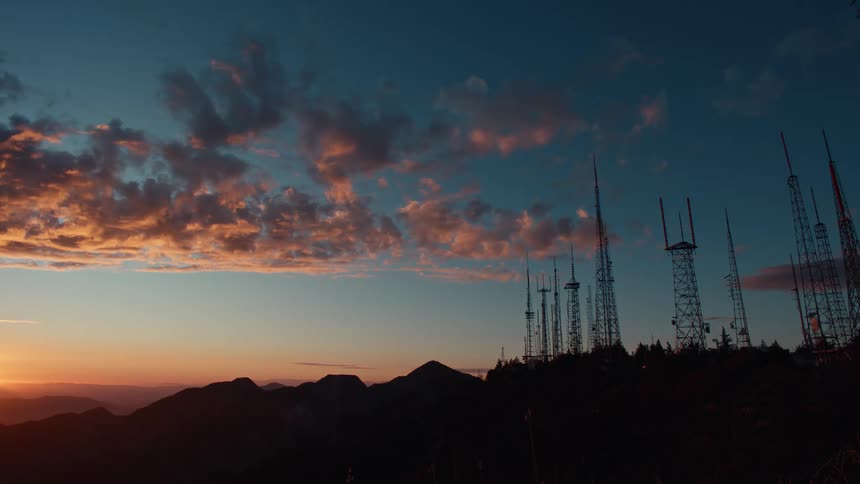 Communication towers stand out against the sky painted by the sunset