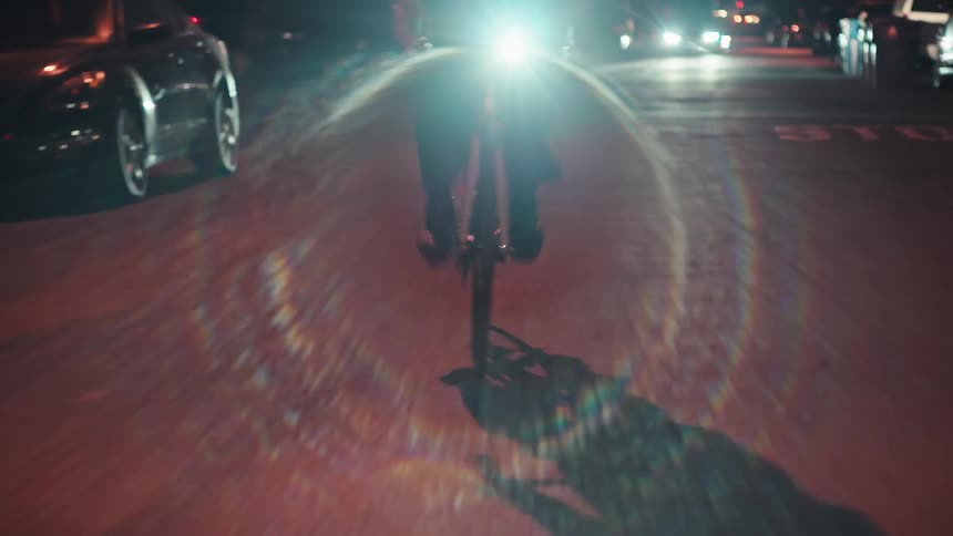 A flashlight attached to the front of a bicycle with a person riding on a street at night