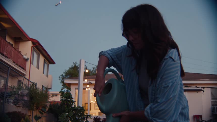 A woman using a watering can to water the plants in her backyard on a sunny day