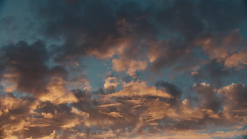 A blue sky with several white clouds and a part of it shining with the orange light of the morning sun