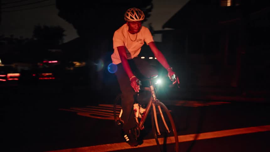 Cyclist rides at night with the bike light on along a lit street