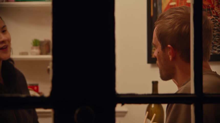 A man and woman eating in a house filmed through a window