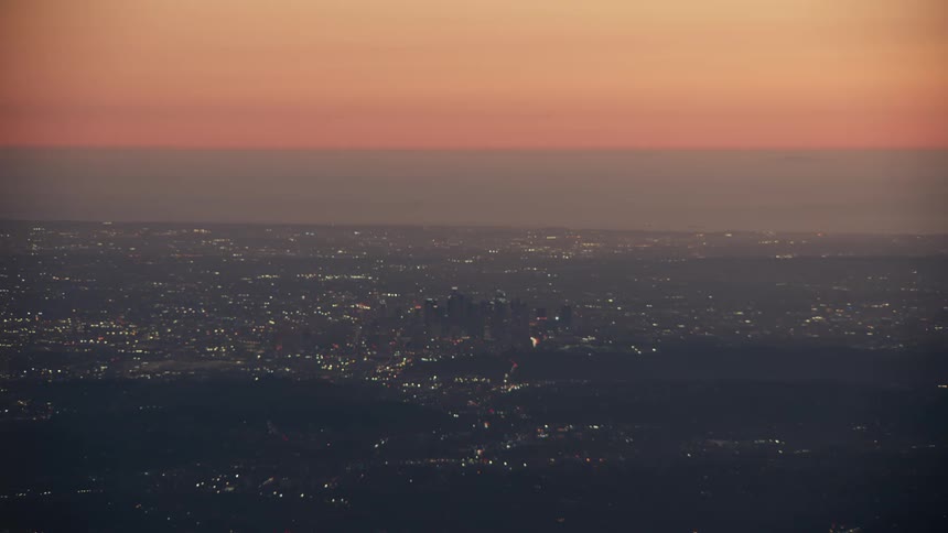 A vast dark landscape of city lights stretching across the terrain and meeting the horizon all dominated by a brilliant sky