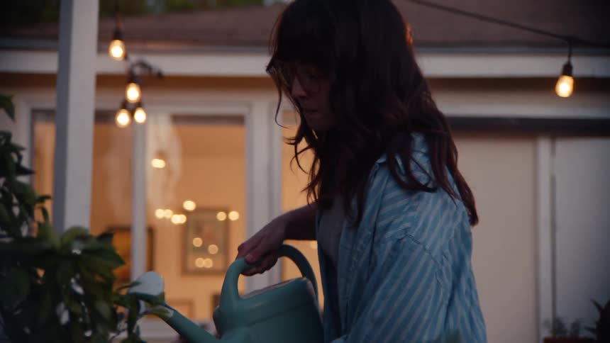 Woman waters plants in the backyard at dusk
