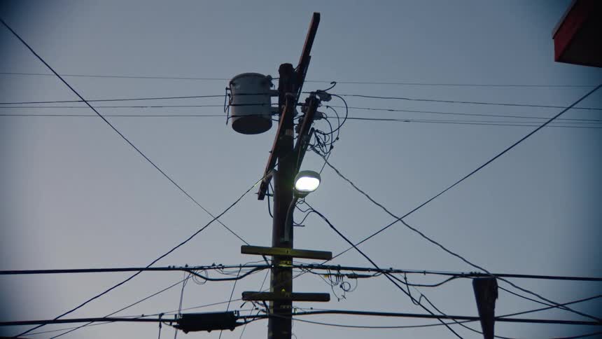 Cables on a utility pole next to a residential building as the street light goes out