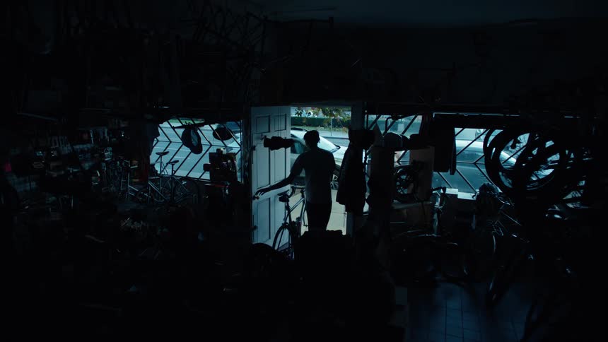 Man turns off the shop light and pushes the bicycle out the door