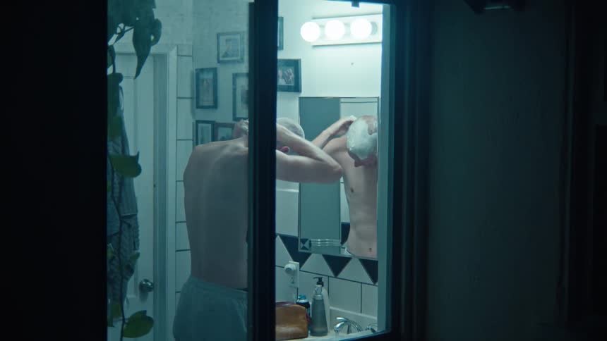 A view through a window of a man shaving his head