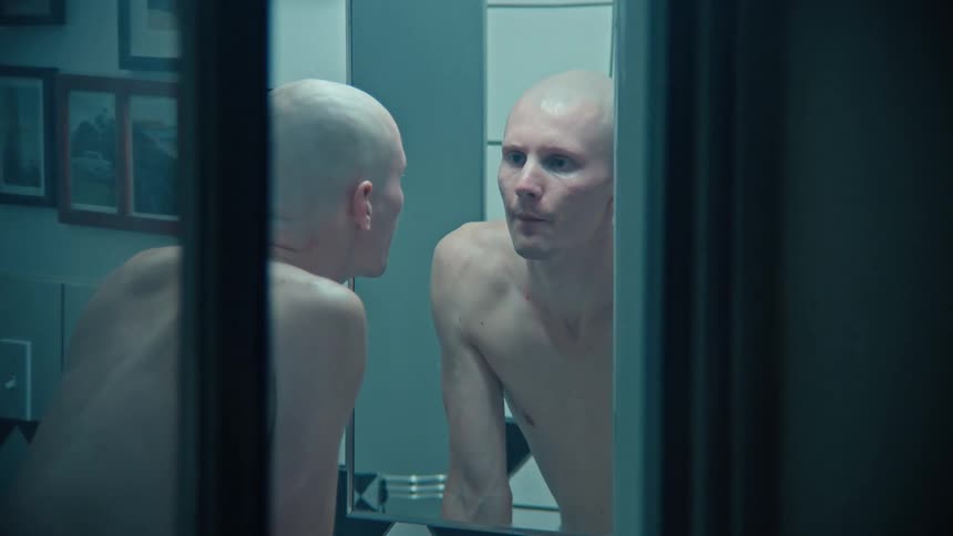 The man wets his face and looks in the mirror