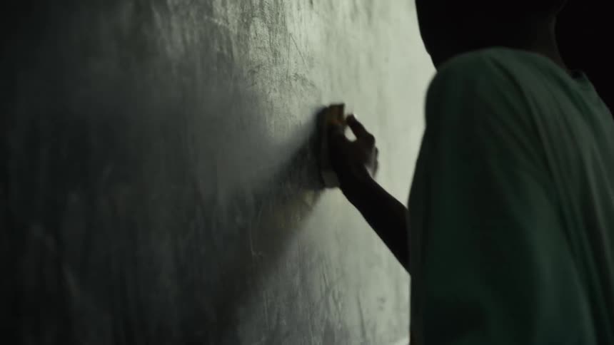 A person is seen from behind wearing a lightcolored shirt in a dimly lit space they are rubbing a small round object against a dark textured wall possibly cleaning or polishing it