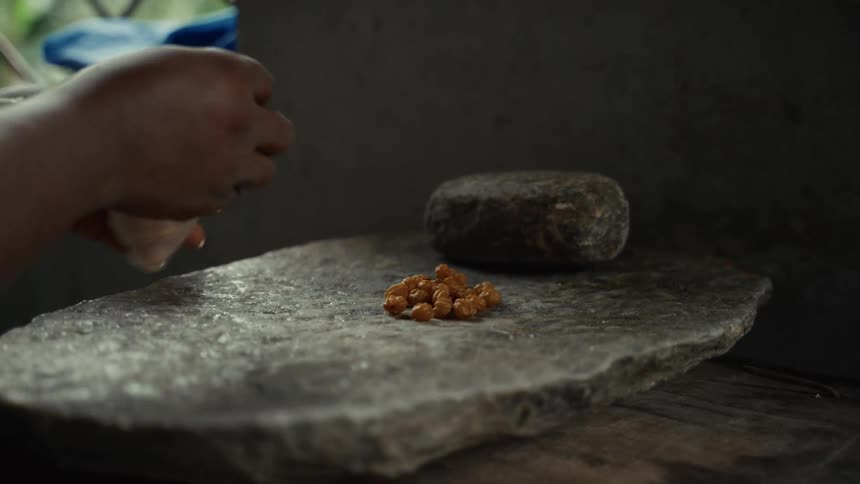 A person has poured nuts onto a stone slab and is tying up the rest in a bag