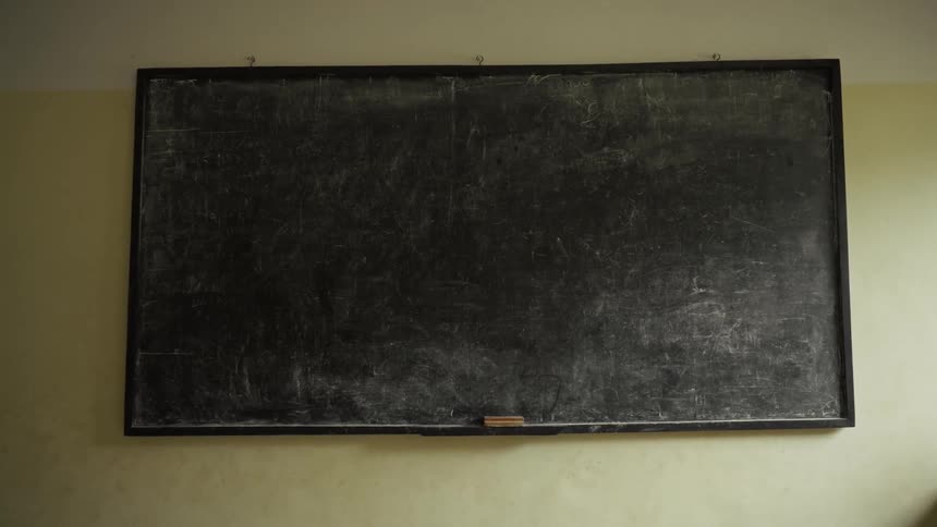 A large chalkboard with chalk dust on the board hangs on a tan wall