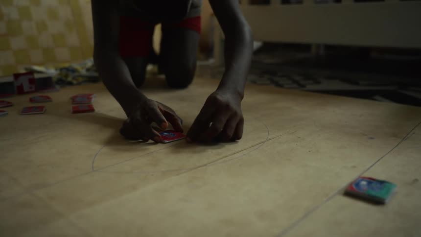 Kneeling on the floor a person flicks small colorful game cards along a hand drawn track